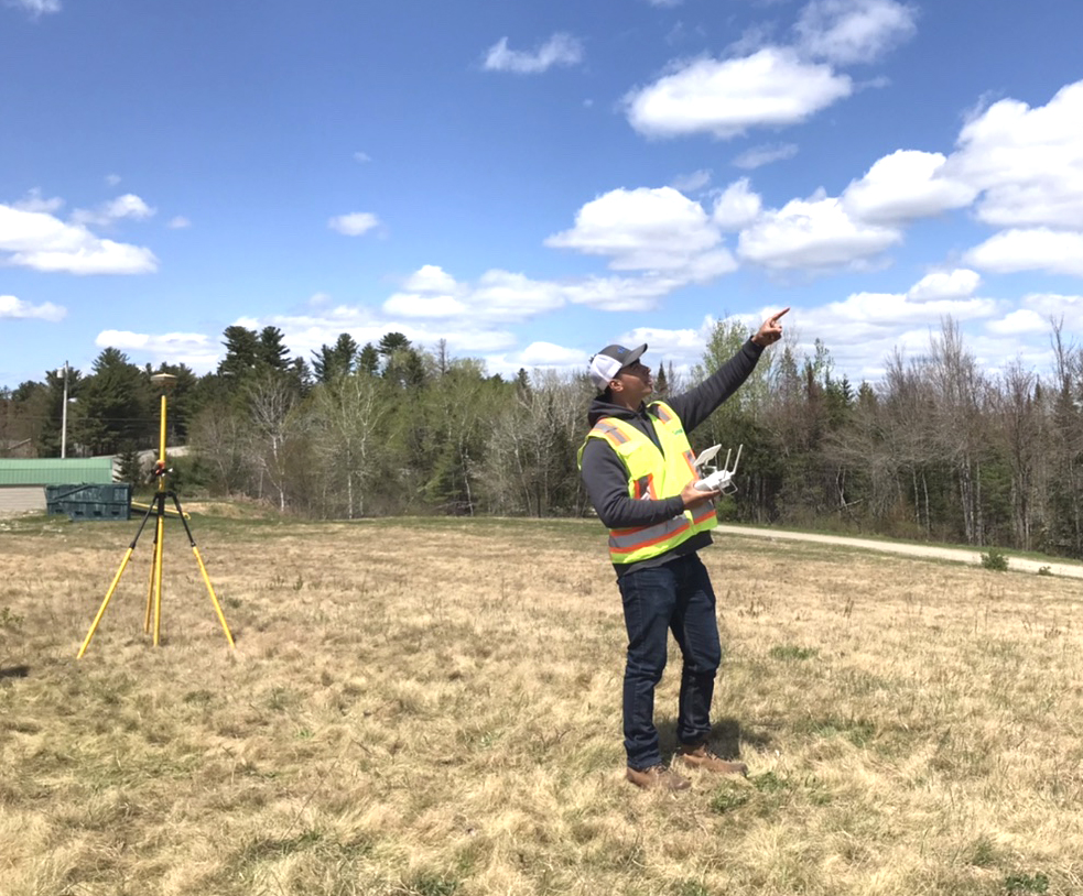 Drone pilot Quinn Stamps scans the sky for its location. An RTK mobile base station seen on the left provides real-time GPS corrections to the drone as it is flying and collecting images.